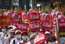 FILE - Anti-coup protesters hold up signs calling on others to join the CDM (Civil Disobedience Movement) during a rally near the Mandalay Railway Station in Mandalay, Myanmar, Feb. 22, 2021.