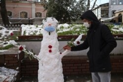 Un joven adorna un muñeco de nieve con una mascarilla en Estambul, el lunes 18 de enero de 2021. La nieve cubrió la mayor parte de la metrópolis turca de unos 16 millones de habitantes que se extiende por dos continentes.