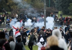 FILE - Demonstrators react as a stun grenade explodes during an opposition rally to reject the presidential election results in Minsk, Belarus, Oct. 11, 2020.