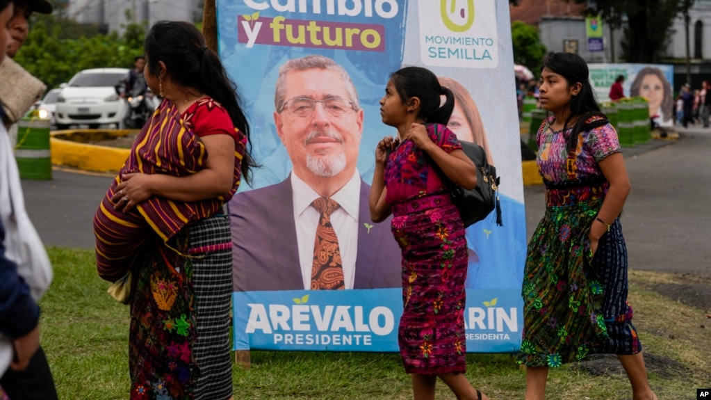 Varias personas pasan frente a un cartel electoral del candidato Bernardo Arévalo, quien encabeza las encuestas para la segunda vuelta de elecciones presidenciales en Guatemala, el 15 de agosto de 2023.