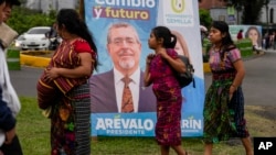 Varias personas pasan frente a un cartel electoral del candidato Bernardo Arévalo, quien encabeza las encuestas para la segunda vuelta de elecciones presidenciales en Guatemala, el 15 de agosto de 2023.