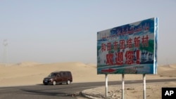 FILE - A car drives through a desert where a signboard which reads "Welcome to the Hotan Unity New Village" is seen on display in Hotan, in western China's Xinjiang region on Sept. 21, 2018. 