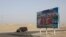 FILE - A car drives through a desert where a signboard which reads "Welcome to the Hotan Unity New Village" is seen on display in Hotan, in western China's Xinjiang region on Sept. 21, 2018. 