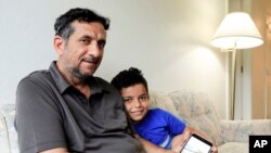 FILE - Hadi Mohammed sits with his 9-year-old son, Sept. 29, 2018, in a Lincoln, Neb., apartment, as he show a photo of his son as a baby in Baghdad. Death threats drove them out of Iraq, but the danger hasn’t been enough to allow his wife to join them.