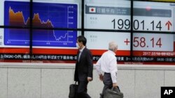 FILE - Men walk past an electronic stock board showing Japan's Nikkei 225 index at a securities firm in Tokyo, May 10, 2017. 