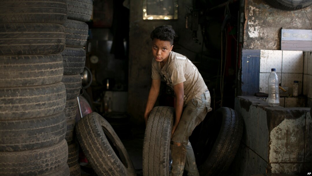 Un niño lleva una llanta hacia un taller de reparación donde trabaja en El Cairo, Egipto, el miércoles, 12 de junio de 2019.