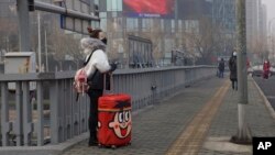 A traveler stands on a bridge near a display showing government propaganda in the fight against the COVID-19 viral illness in Beijing, China Thursday, Feb. 13, 2020. China is struggling to restart its economy after the annual Lunar New Year holiday…