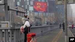 A traveler stands on a bridge near a display showing government propaganda in the fight against the COVID-19 viral illness in Beijing, China, Feb. 13, 2020.