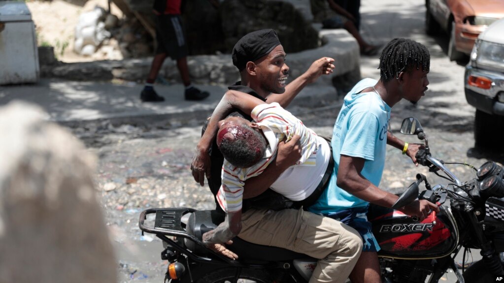 Un agente de policía sostiene a un hombre herido de bala en la cabeza durante choques violentos entre pandillas mientras lo llevan en mototaxi en el distrito Carrefour-Feuilles de Puerto Príncipe, el 15 de agosto de 2023. 