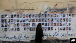 FILE - A Bahraini woman walks past images of political prisoners plastered on a wall in Sanabis, Bahrain, Oct. 22, 2015, 