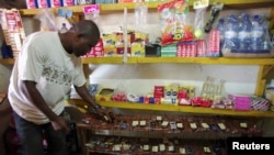 A shopkeeper stands beside mobile phones charging from a generator in Tintafor, Sierra Leone, Sept. 17, 2009