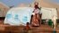 A woman walks past a child playing with water in a refugee camp in Sevare, Mali, Jan. 26, 2013. 