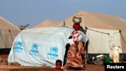 A woman walks past a child playing with water in a refugee camp in Sevare, Mali, Jan. 26, 2013. 