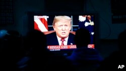 FILE - Migrants mainly from Mexico and Central America watch from a border migrant shelter in Tijuana, Mexico, as U.S. President Donald Trump gives a prime-time address about border security Jan. 8, 2019. 