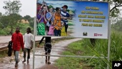 FILE - People walk past a billboard warning residents to stop the stigmatization of Ebola survivors, in Kenema, eastern Sierra Leone, Aug. 12, 2015.