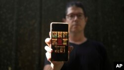 FILE - Yuval Haran, whose family is celebrating the return of his mother, his sister, and four others from Hamas captivity in the Gaza Strip, poses for a portrait with a picture on his phone of his family's hostage posters,in Herziliya, Israel, Decenber. 4, 2023.