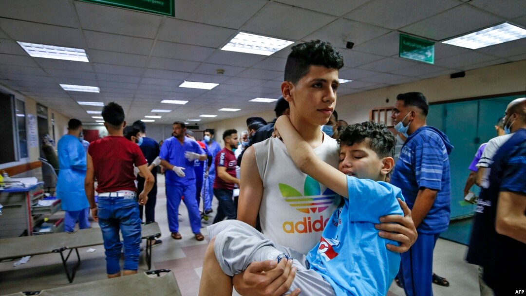 Seorang pemuda Palestina menggendong seorang anak laki-laki, terluka dalam serangan udara Israel, di dalam sebuah rumah sakit di Kota Gaza City pada, 12 Mei 2021. (Foto: AFP)