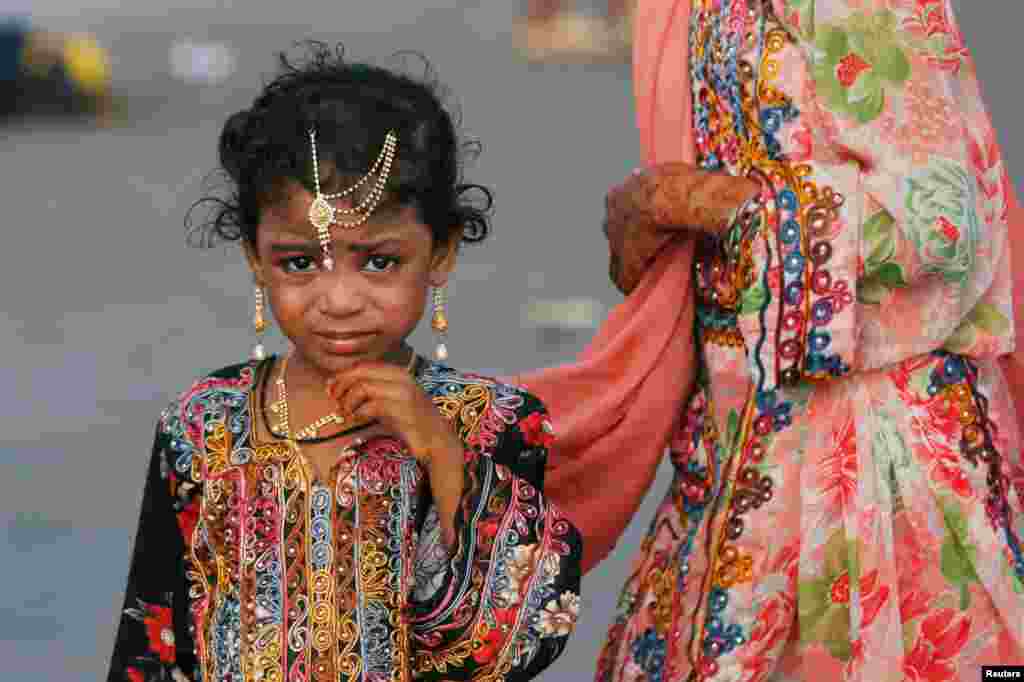 A girl adorned with jewelry wears a traditional dress while walking with her sibling during Eid al-Fitr celebrations, at Clifton beach in Karachi, Pakistan.