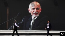 People walk near a mural of President Ashraf Ghani at Hamid Karzai International Airport, in Kabul, Afghanistan, Saturday, Aug. 14, 2021. As a Taliban offensive encircles the Afghan capital, there's increasingly only one way out for those fleeing…