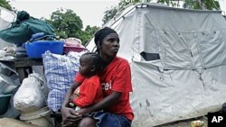 A woman displaced due to the Jan 12, 2010 earthquake holds a child as she rests next to her tent and belongings before leaving the refugee camp at the Saint Pierre park in Port-au-Prince, Haiti, Dec 14, 2010