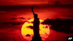 FIL - The sun sets behind the Statue of Liberty, Nov. 17, 2022, in New York. Foreign students seeking visas to study in the United States can face long waits. 
