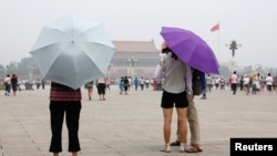 Pengunjung ke Lapangan Tiananmen melindungi diri dari matahari dengan payung di hari yang panas dan berkabut di Beijing. (Foto: Reuters)