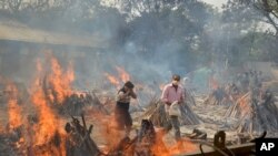 Relatives react to heat emitting from the multiple funeral pyres of COVID-19 victims at a crematorium in the outskirts of New Delhi, India, Apr. 29, 2021. 