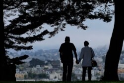 FILE - A man and woman walk under trees down a path at Alta Plaza Park in San Francisco, July 3, 2017.