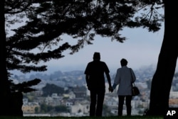 FILE - A man and woman walk under trees down a path at Alta Plaza Park in San Francisco, July 3, 2017.