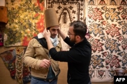 FILE - Yunus Girgic (R) adjusts as he delivers a symbolic hat "Sikke", worn by whirling dervishes, to his customer Ashmi Benmehidi (L), a French musician who left an insurance job in Montpellier, South of France, to practice the art of the ney, in Konya on December 17,2023.