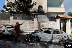 Seorang pria berdiri di samping mobil-mobil yang terbakar sambil menunjuk kerusakan di rumahnya, sehari setelah serangan oleh pemukim Yahudi di desa Jit dekat Nablus di Tepi Barat yang diduduki. (Foto: AFP)