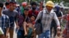 Anti-coup protesters carry an injured man following clashes with security in Yangon, Myanmar Sunday, March 14, 2021. The civilian leader of Myanmar's government in hiding vowed to continue supporting a "revolution" to oust the military that seized…