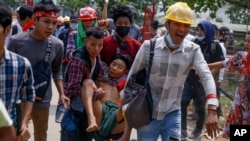 Anti-coup protesters carry an injured man following clashes with security in Yangon, Myanmar Sunday, March 14, 2021. The civilian leader of Myanmar's government in hiding vowed to continue supporting a "revolution" to oust the military that seized…