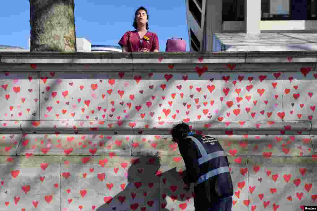 A health worker from St. Thomas&#39; hospital stands behind a wall being painted in hearts as a memorial to all those who have died so far in the UK from COVID-19, amid the pandemic in London.