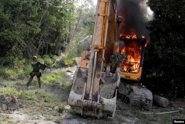 FILE PHOTO: An agent of the Brazilian Institute for the Environment and Renewable Natural Resources (IBAMA) throws oil at a machine to destroy it at an illegal gold mine during an operation ran jointly with the Federal Police near the city of Altami, Para state, Brazil on August 30, 2019. (REUTERS/Nacho Doce/File Photo)