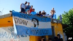 Fans stand on a roof of a house along the route of the motorcade carrying the remains of football star Diego Maradona to the Jardin de Bellavista cemetery in Buenos Aires, Argentina, Nov. 26, 2020. 