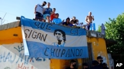 Para penggemar sepak bola berdiri di atap rumah di sepanjang rute yang dilalui rombongan yang membawa jenazah pesepak bola legendaris Diego Maradona ke pemakaman Jardin de Bellavista di Buenos Aires, Argentina, 26 November 2020. 