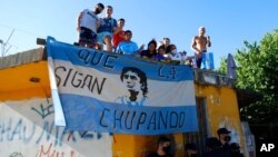 Para penggemar sepak bola berdiri di atap rumah di sepanjang rute yang dilalui rombongan yang membawa jenazah pesepak bola legendaris Diego Maradona ke pemakaman Jardin de Bellavista di Buenos Aires, Argentina, 26 November 2020. 