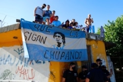 អ្នក​គាំទ្រកីឡាករ​បាល់ទាត់​លោក Diego Maradona ឈរ​នៅ​លើ​ដំបូល​ផ្ទះ​ខណៈ​ក្បួន​ម៉ូតូ​ដង្ហែ​សព្វ​លោក​នៅ​ក្នុងរដ្ឋធានីប៊ុយណូស៊ែ ប្រទេស​អាហ្សង់ទីន កាល​ពី​ថ្ងៃ​ទី​២៦ ខែ​វិច្ឆិកា ឆ្នាំ​២០២០។ ​(AP)