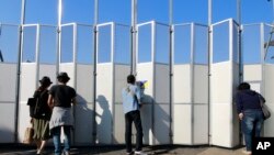 FILE - People peep in the site of the new national stadium, which will host the opening and closing ceremonies and track and field of the 2020 Tokyo Olympics, in Tokyo.