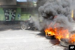 FILE —A motorcyclist rides past burning tires during a protest to demand the resignation of the Prime Minister Ariel Henry in Port-au-Prince, Haiti, March 1, 2024.