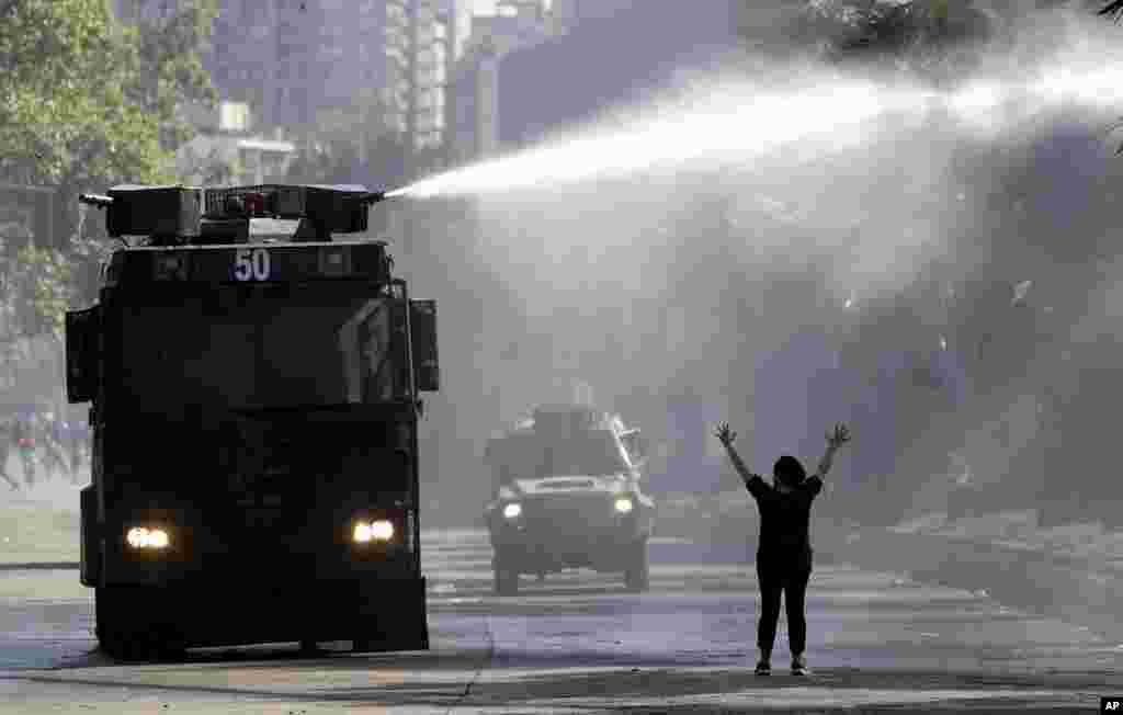 Una manifestante levanta las manos hacia un camión de la policía que rocía un cañón de agua contra estudiantes y miembros del sindicato que marchaban en Santiago, Chile, el lunes 21 de octubre de 2019. (AP Photo / Miguel Arenas).