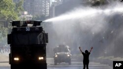 Una manifestante chilena levanta sus brazos en desafío de un cañón de agua de los militares que intentan mantener vigente un estado de emergencia para poner fin a las protestas que han dejado ya 18 muertos. 