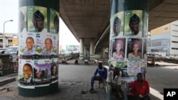 Men take a rest under a bridge pasted with election posters in Lagos, Nigeria, March 30, 2011