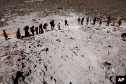 People carry luggage as they cross into Syria on foot through a crater caused by Israeli airstrikes aiming to block Beirut-Damascus highway at the Masnaa crossing, in the eastern Bekaa Valley, Lebanon, Oct. 5, 2024.