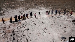 People carry their luggage as they cross into Syria on foot through a crater caused by Israeli airstrikes aiming to block Beirut-Damascus highway at the Masnaa crossing, in the eastern Bekaa Valley, Lebanon, Oct. 5, 2024. 