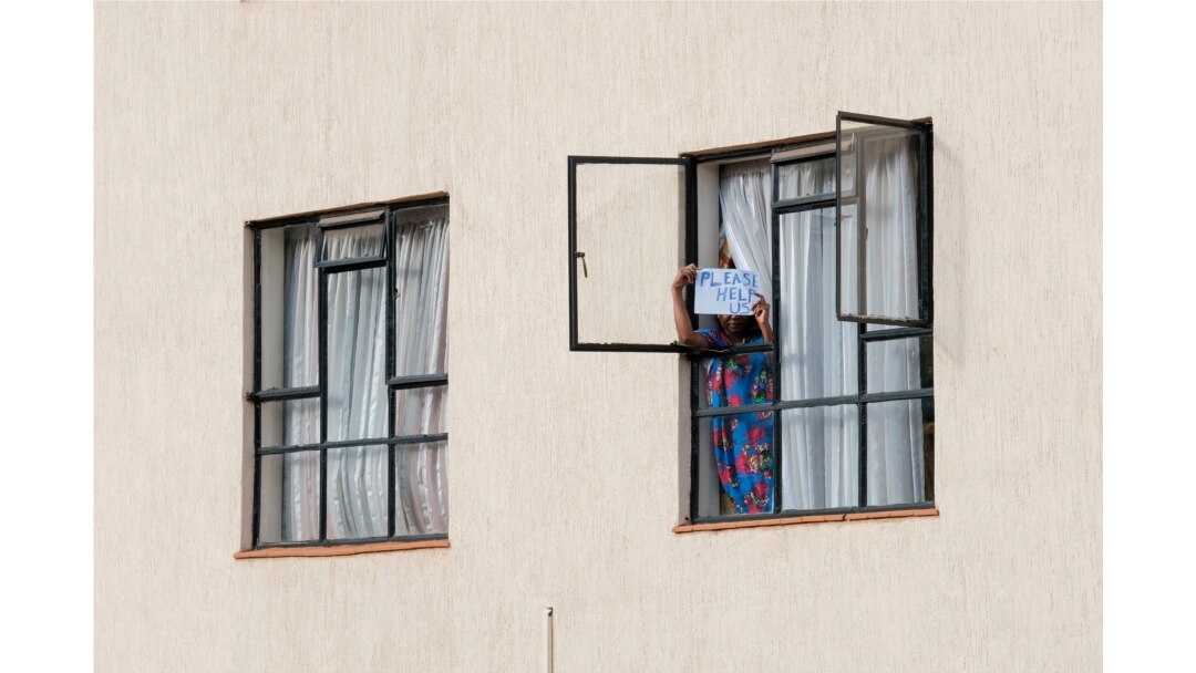 FILE - A young lady holds a sign asking for help after the Ministry of Health extended the detention period of people in quarantine to 28 days at a government-designated quarantine facility in Nairobi, April 4, 2020.