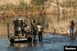 Sebuah keluarga migran dijemput oleh anggota Departemen Keamanan Publik Texas setelah terdampar di tepi sungai selama berjam-jam, di Eagle Pass, Texas, terlihat dari Piedras Negras, Meksiko pada 18 Januari 2024. (REUTERS/Go Nakamura)