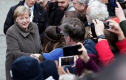 German Chancellor Angela Merkel, left, shakes hands with visitors prior to a memorial service in the chapel at the Berlin Wall Memorial in Berlin, Germany, Nov. 9, 2019.