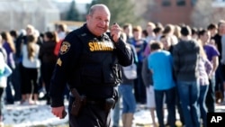 A sheriff deputy talks on his radio at Arapahoe High School where authorities say a student shot at least one other student before he apparently killed himself, in Centennial, Colorado, Dec. 13, 2013.